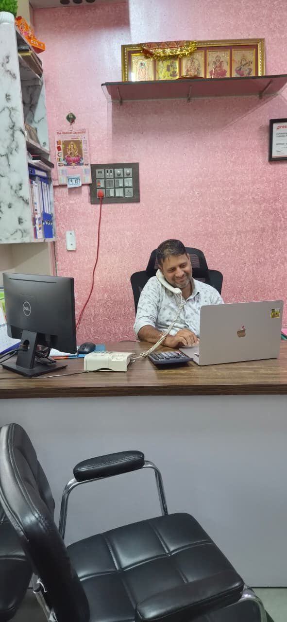 Narayan Mali at his desk in the shop office, on the phone with a laptop open
